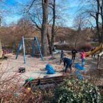 Schaukelbereich auf einem Spielplatz mit Personen die aufräumen
